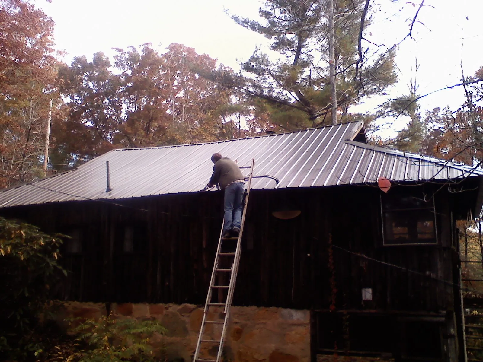 Roofer on a ladder working along the edge of a cabin metal roof in Prospect